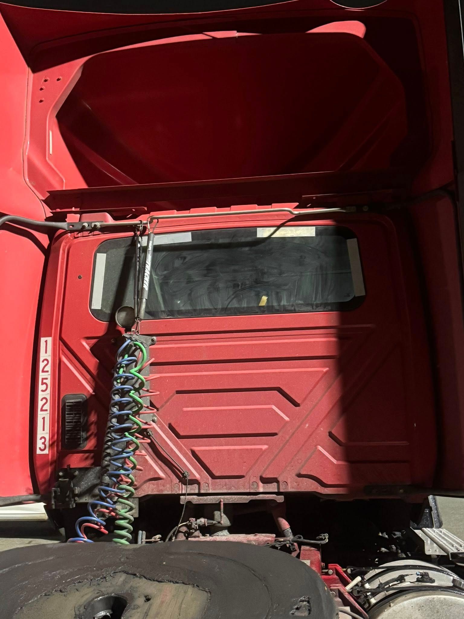 Rear view of a red semi-truck cab with coiled air lines connecting to the trailer hitch area.