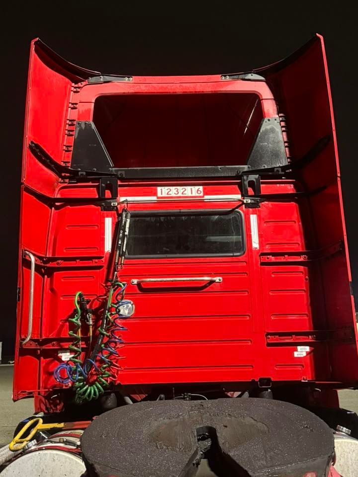 A close-up view of the back of a red semi-truck cabin, featuring a window, air lines, and the fifth-wheel hitch.