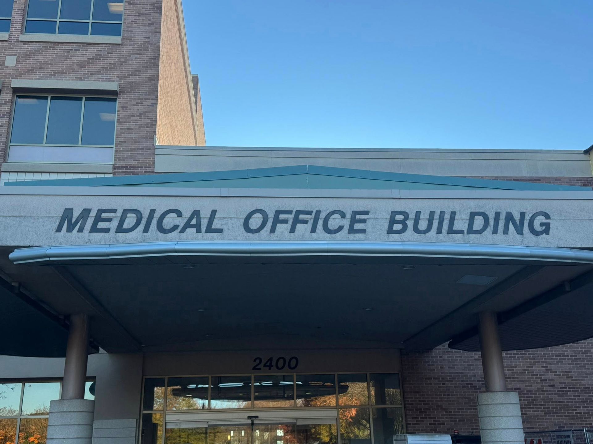 Entrance to a brick Medical Office Building with the address 2400 above the glass doors under a blue overhang.