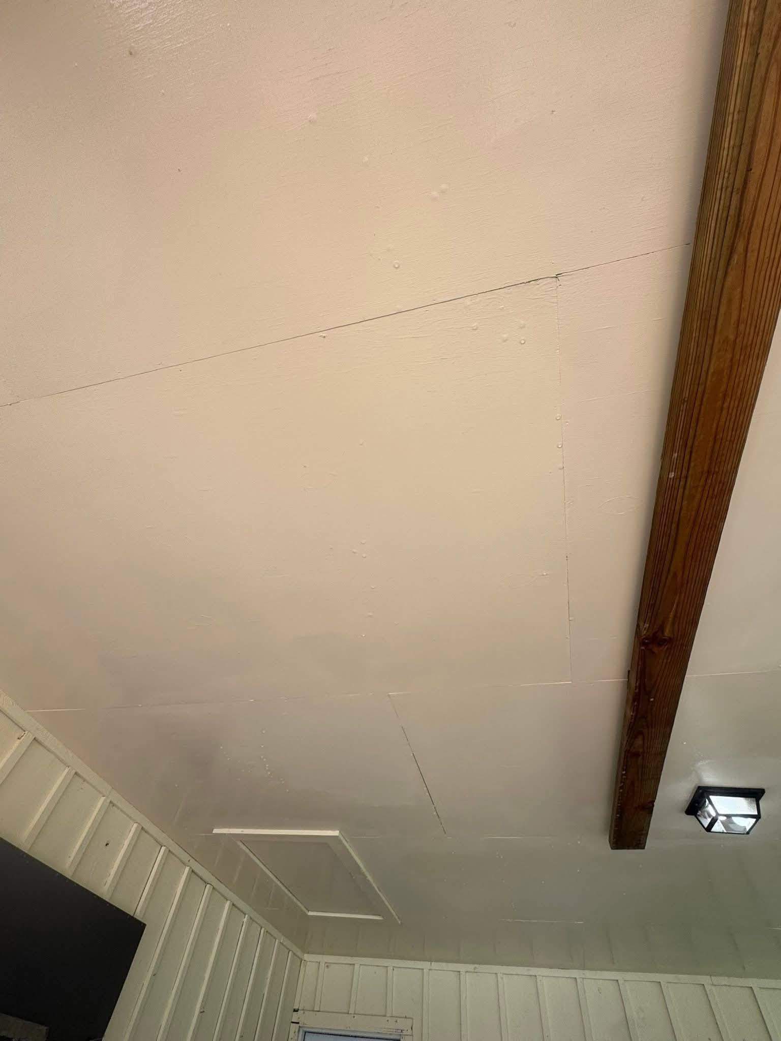 A ceiling showing a rectangular drywall patch with visible seam lines and a nearby attic access panel.