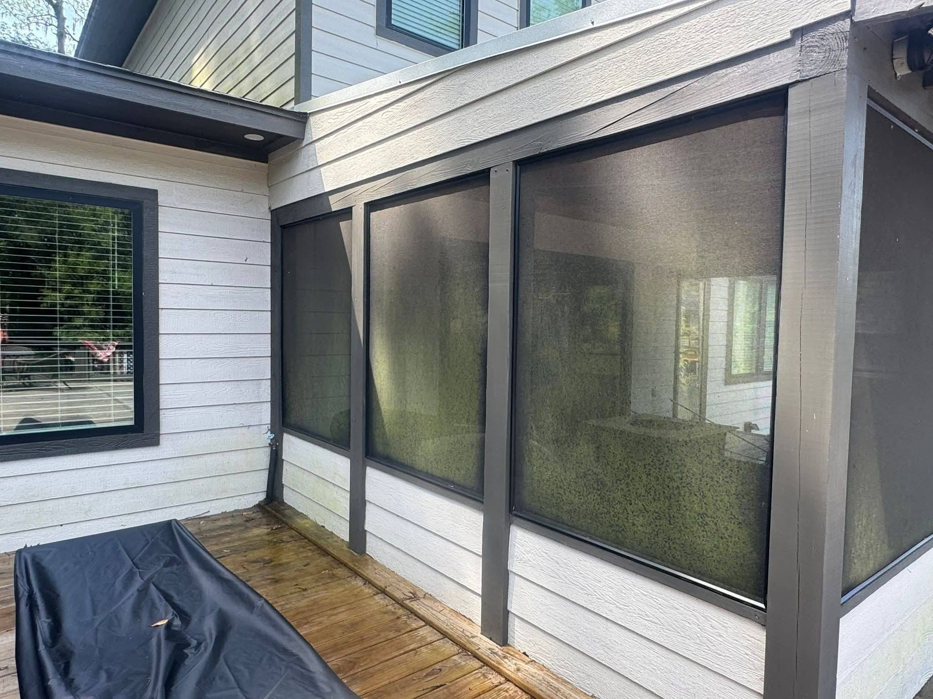 An outdoor wooden deck featuring a screened-in porch with white siding and dark gray framing.