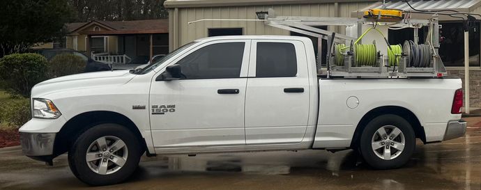 A white Ram 1500 crew cab pickup truck parked outdoors, featuring a specialized equipment rack with hoses in the truck bed.