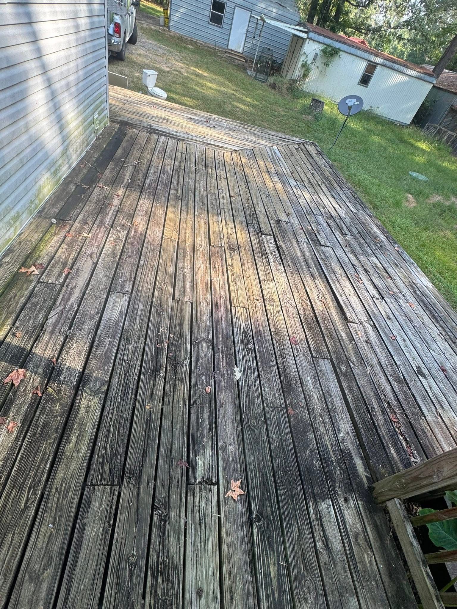 An old, weathered wooden deck with significant dark stains and mildew, situated outside a house next to a grassy yard.