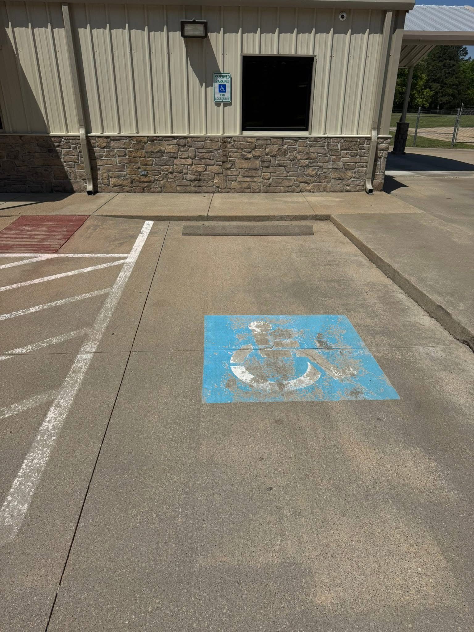 A blue and white wheelchair symbol painted on a paved parking space next to a building.