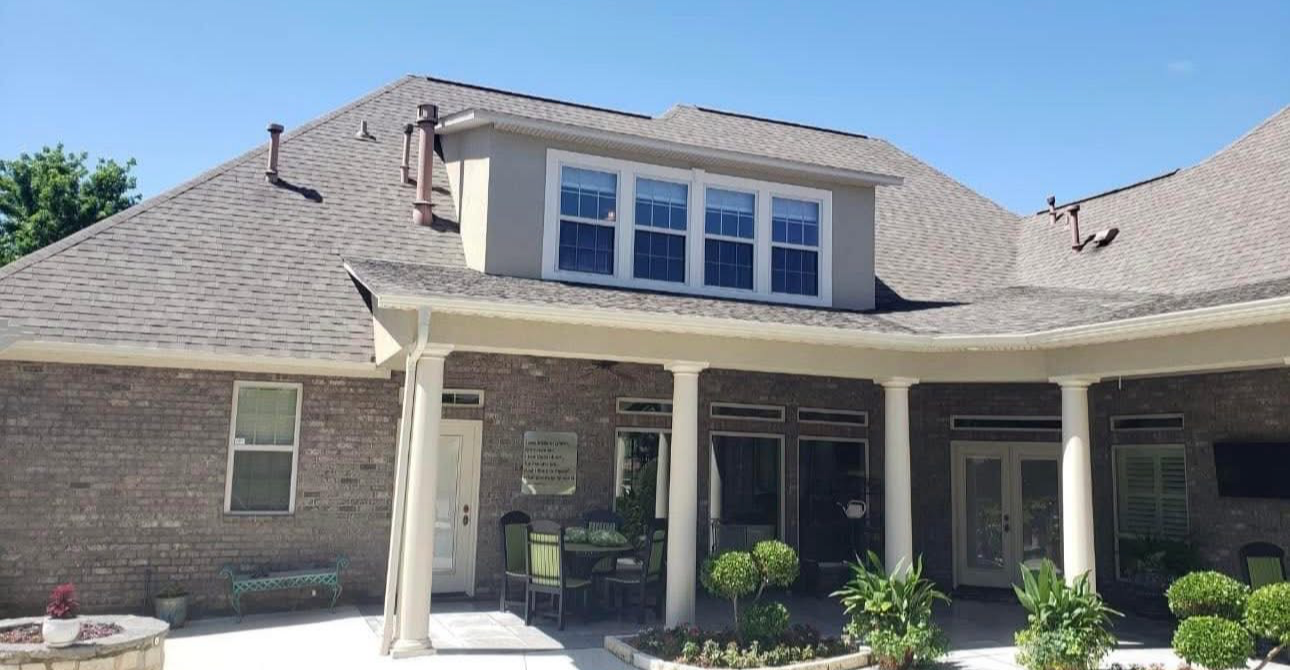 The rear view of a brick house with a covered patio, multiple white columns, and a dormer window above.