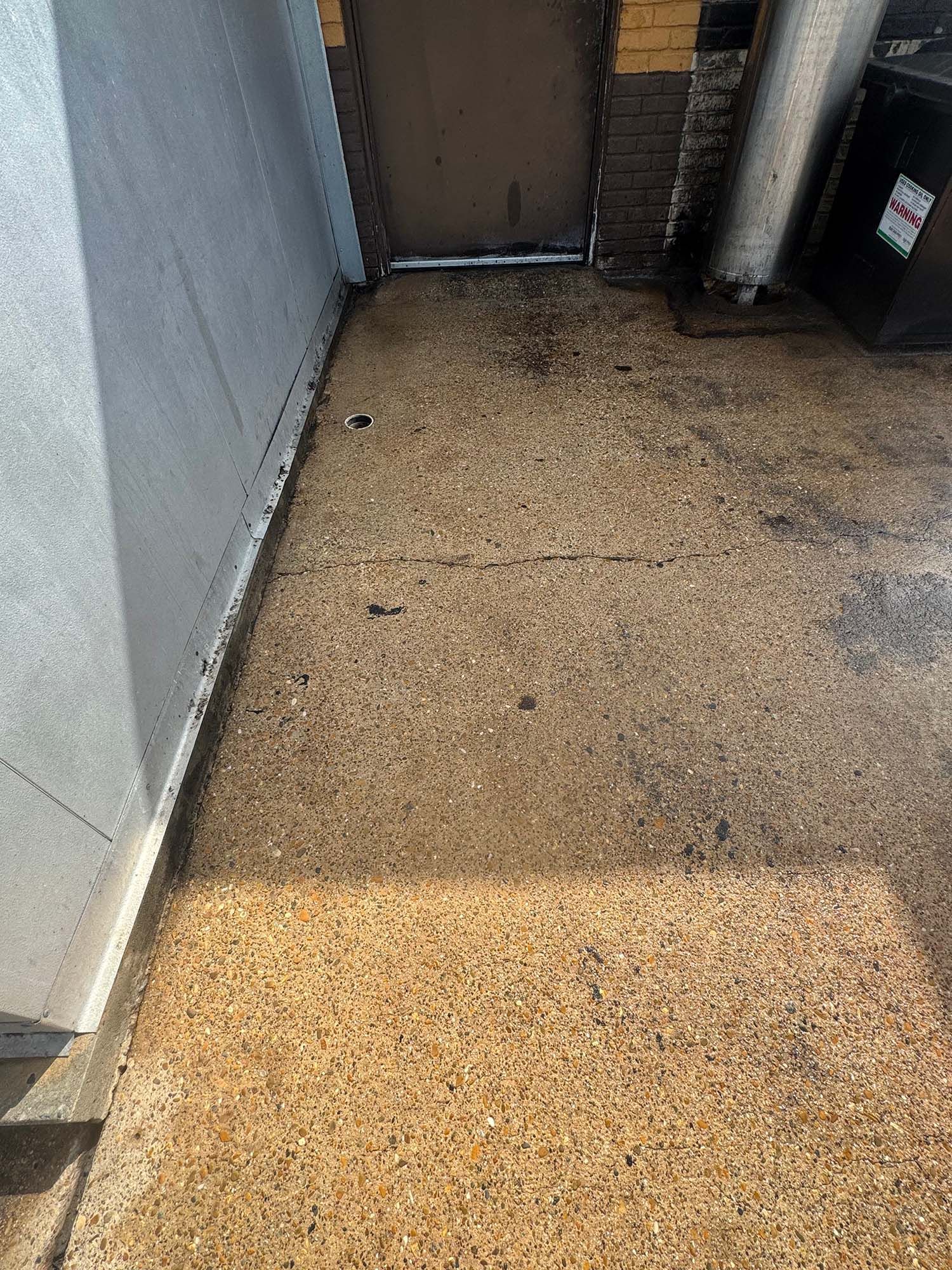 Sunlit concrete walkway with a closed door and trash cans at the end.