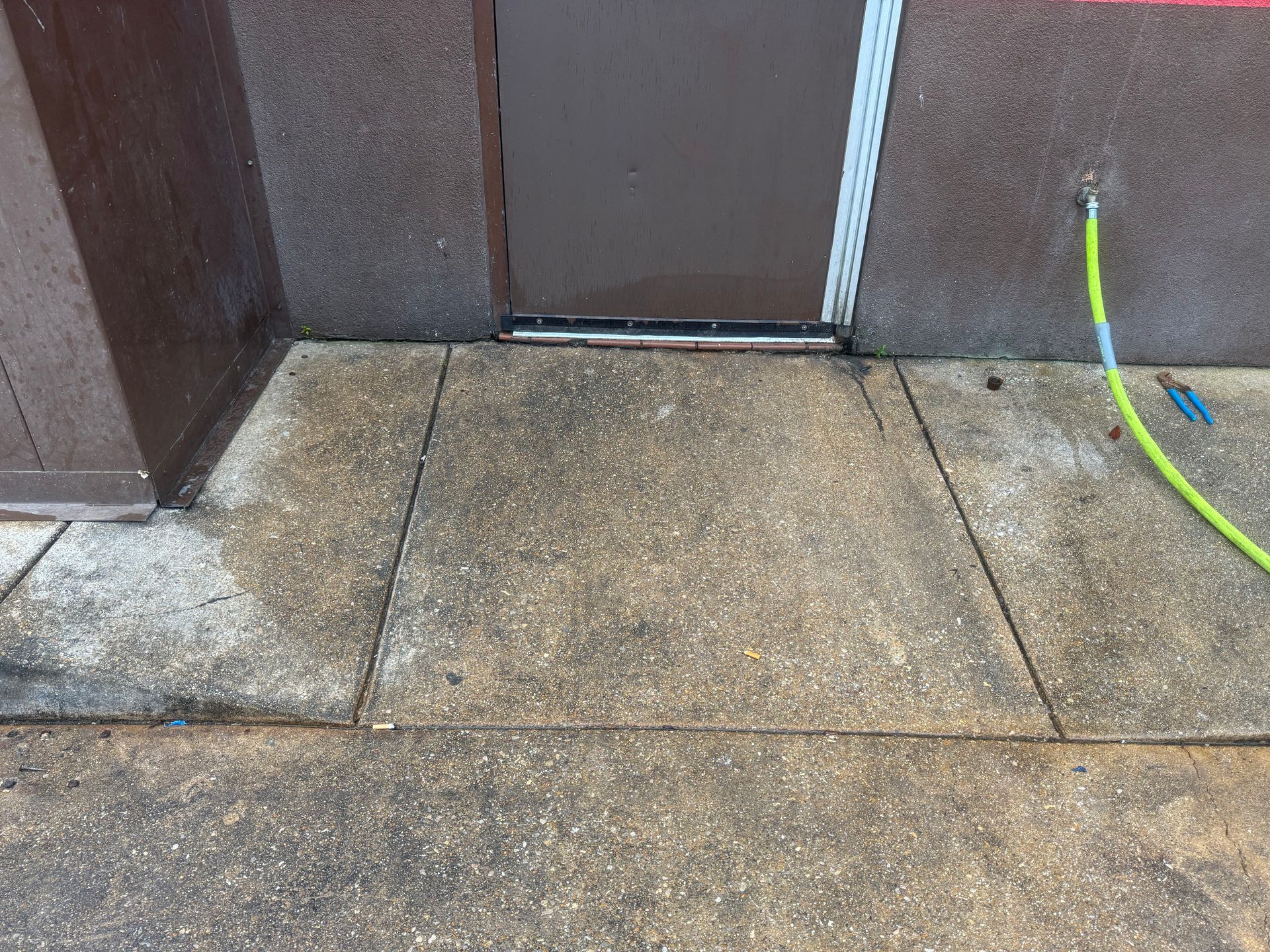 Weathered concrete sidewalk at a doorway, with a green hose along the right wall.