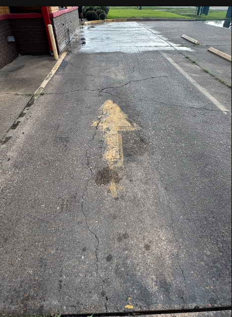 A concrete area between a beige wall and large green dumpsters, showing significant dark staining and wet patches on ground.