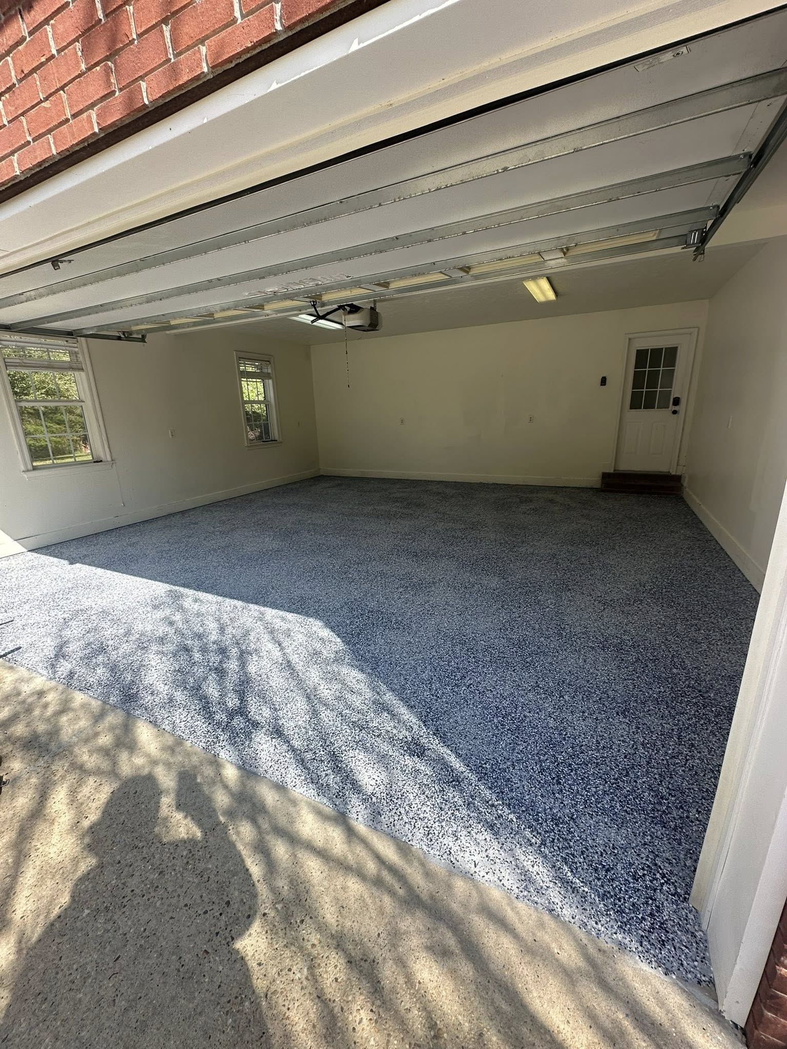 Open garage with blue gravel floor, white walls, and partially raised garage door.