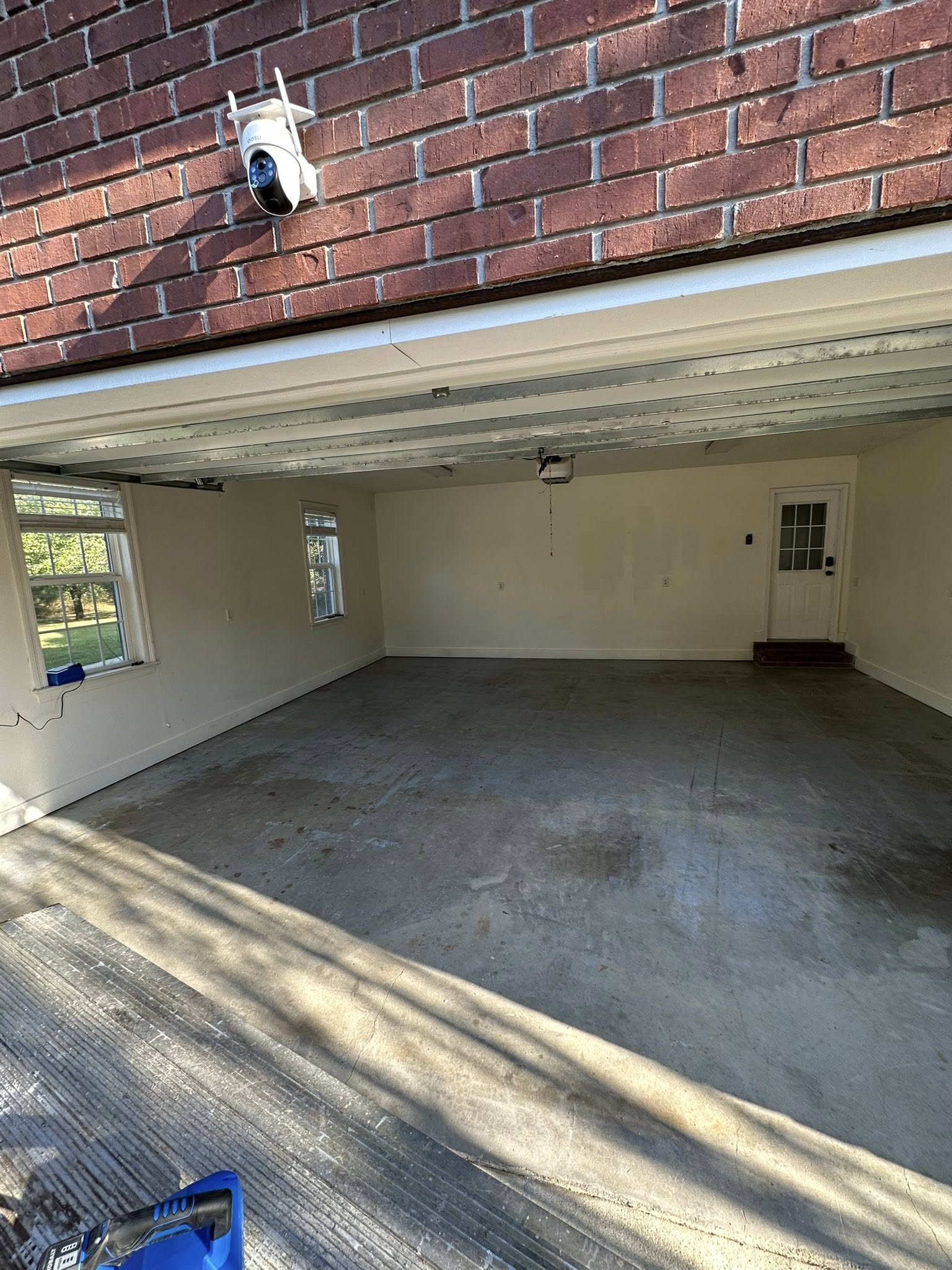 Open garage with concrete floor, brick exterior, and a sunlit interior.