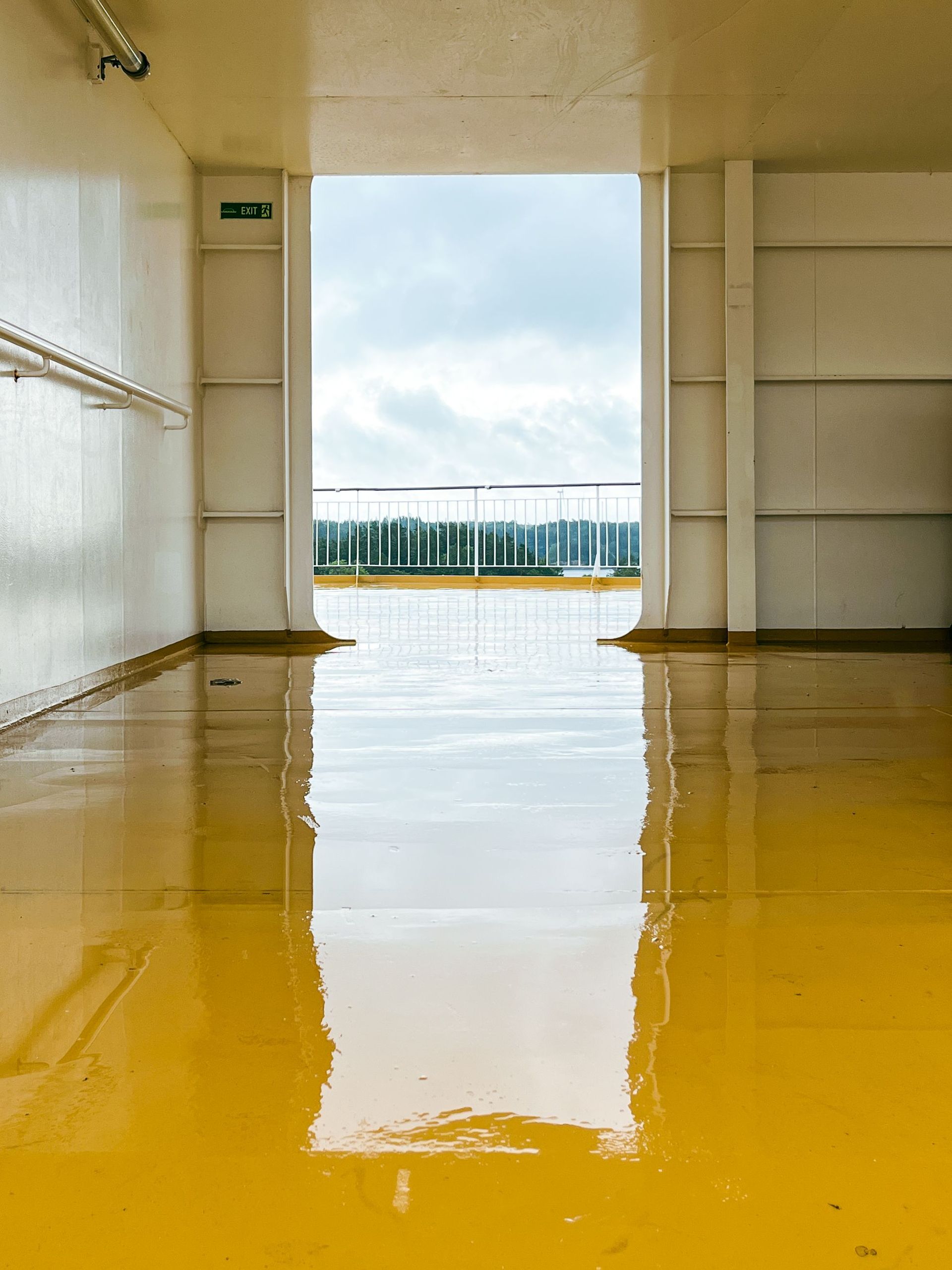 Yellow indoor floor reflecting a bright doorway and cloudy sky beyond