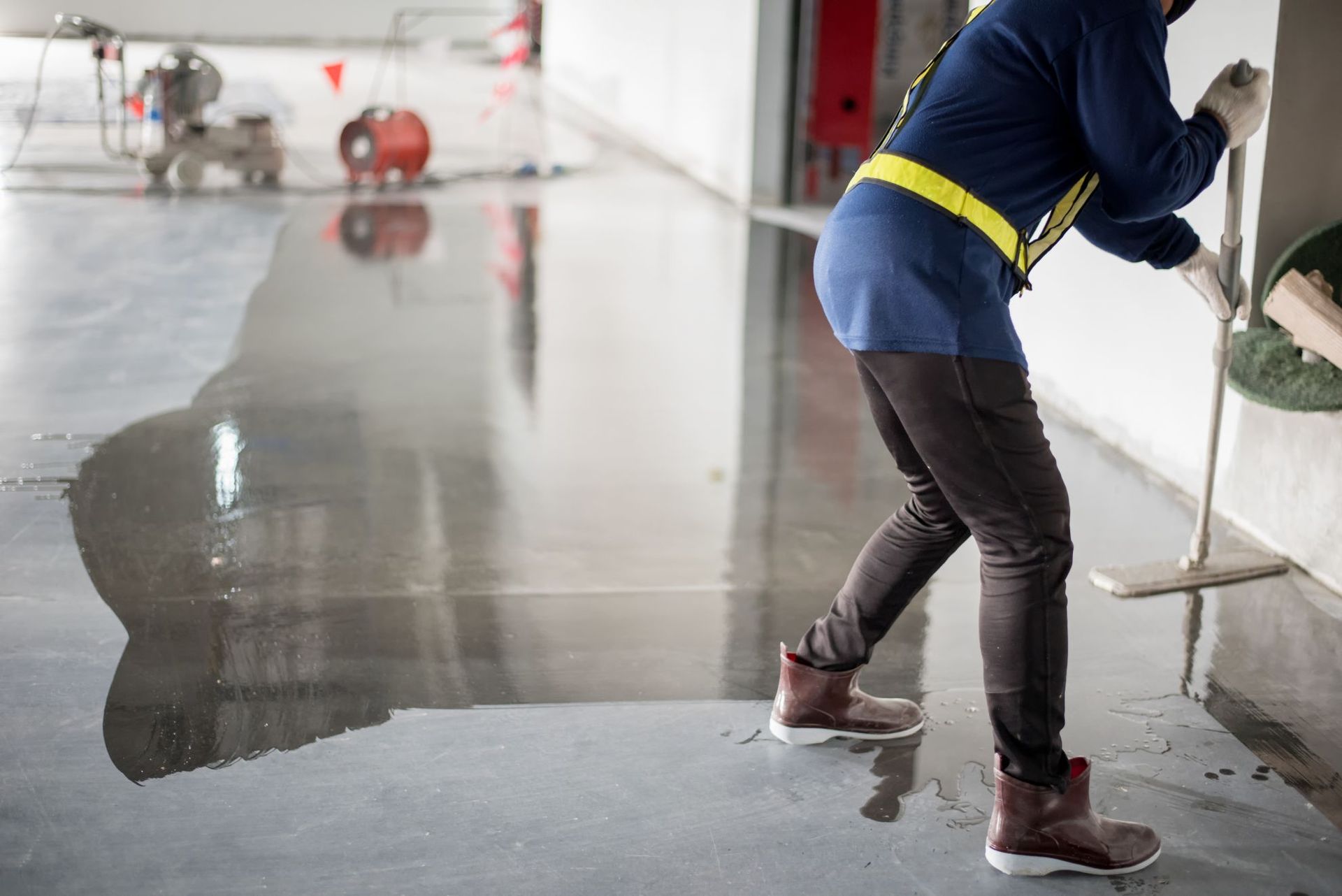 Person mopping water on a wet concrete floor in an indoor industrial space
