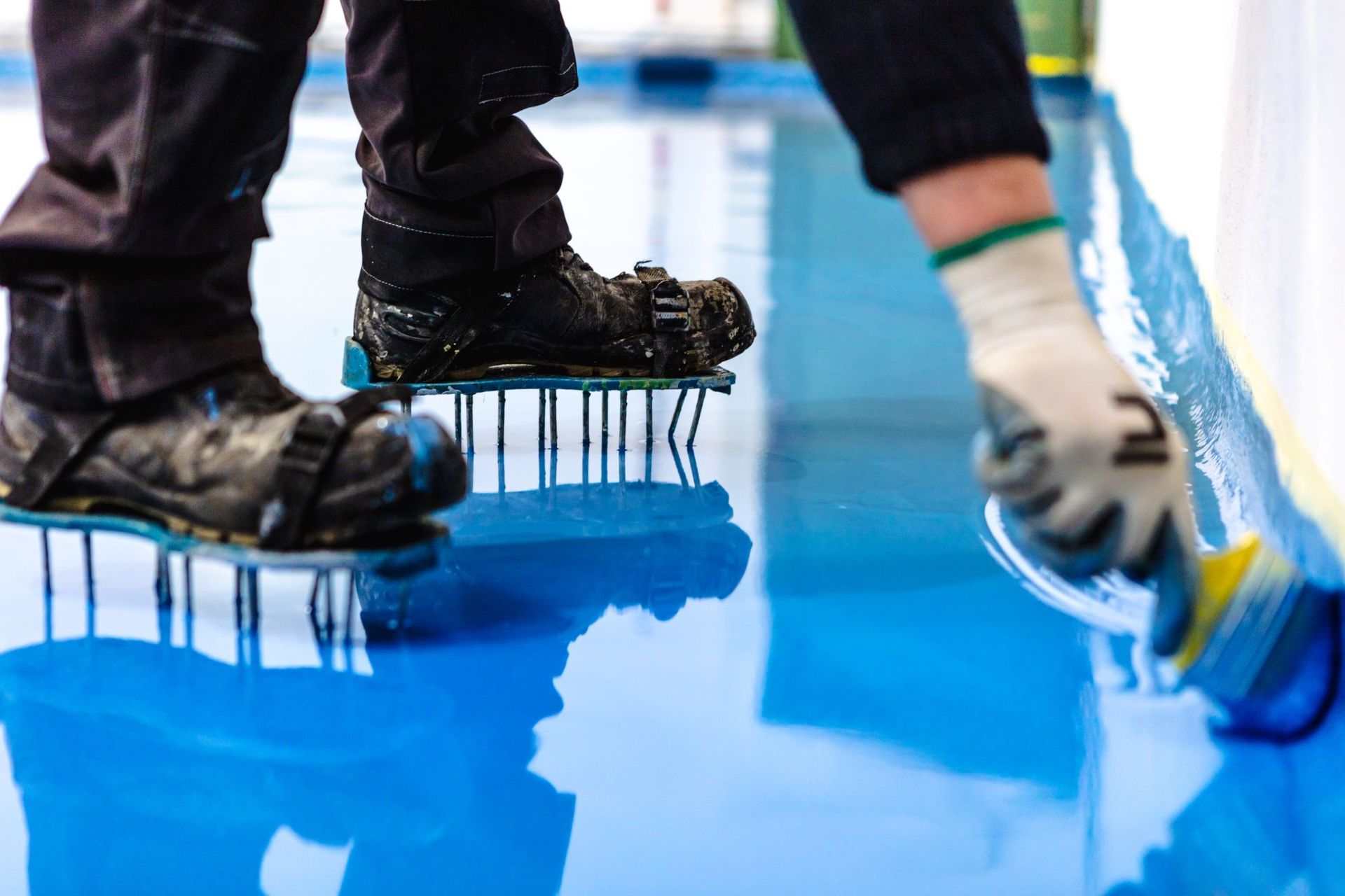 Workers applying bright blue floor coating with rollers and boots visible close-up