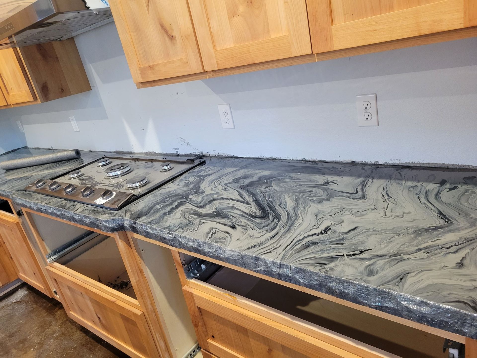 Kitchen with unfinished countertops, gray marbled surface, and cabinets under a wall with outlets