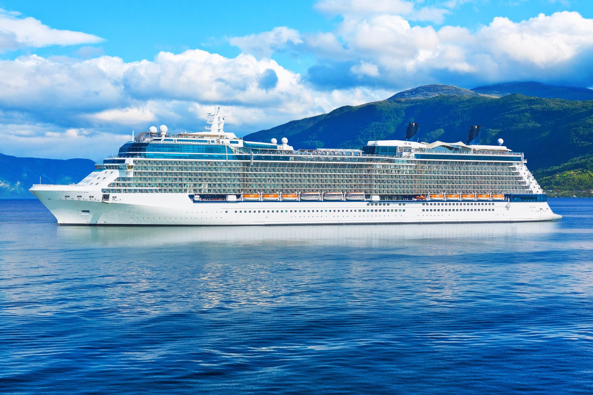 Crucero en aguas azules con montañas al fondo, bajo un cielo azul con nubes.