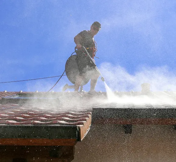 A man is cleaning a tiled roof with a high pressure washer