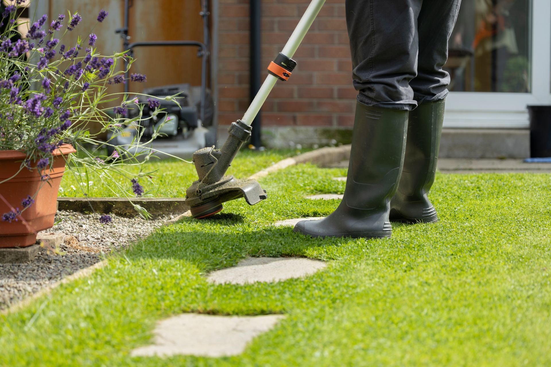 Person edging a lawn with a trimmer beside a house and flower pots