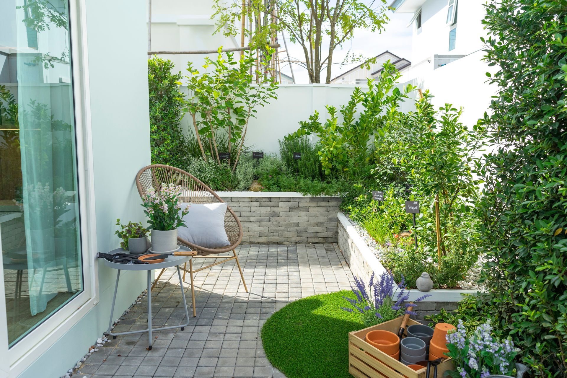 Modern patio with white walls, potted plants, patio chairs, and a small raised garden bed in sunlight
