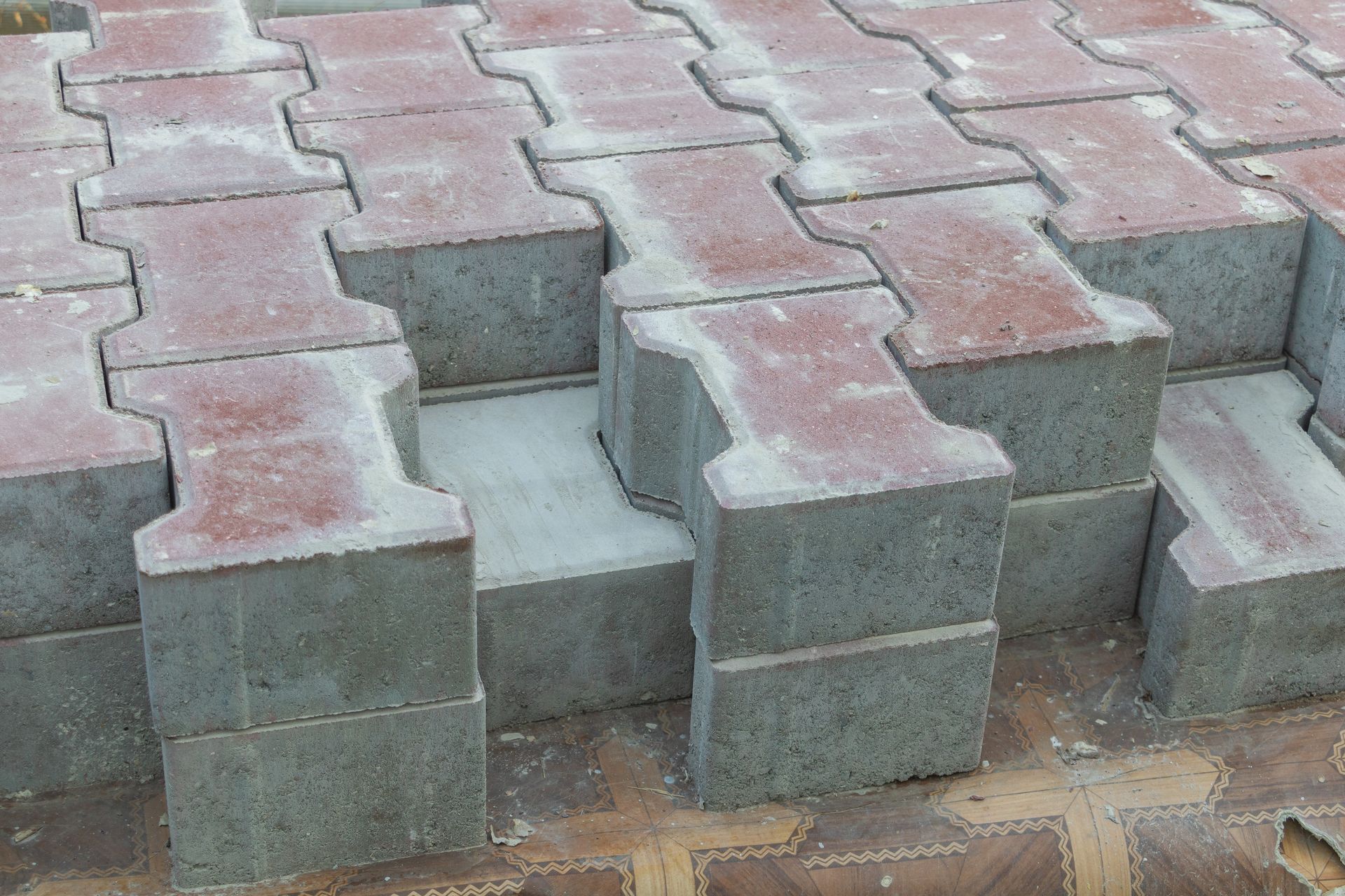 Stacked concrete and red paving blocks forming an unfinished interlocking walkway pattern