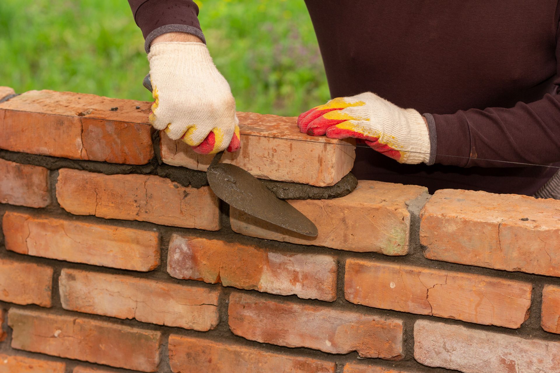 Hands in work gloves spreading mortar on a brick wall during construction