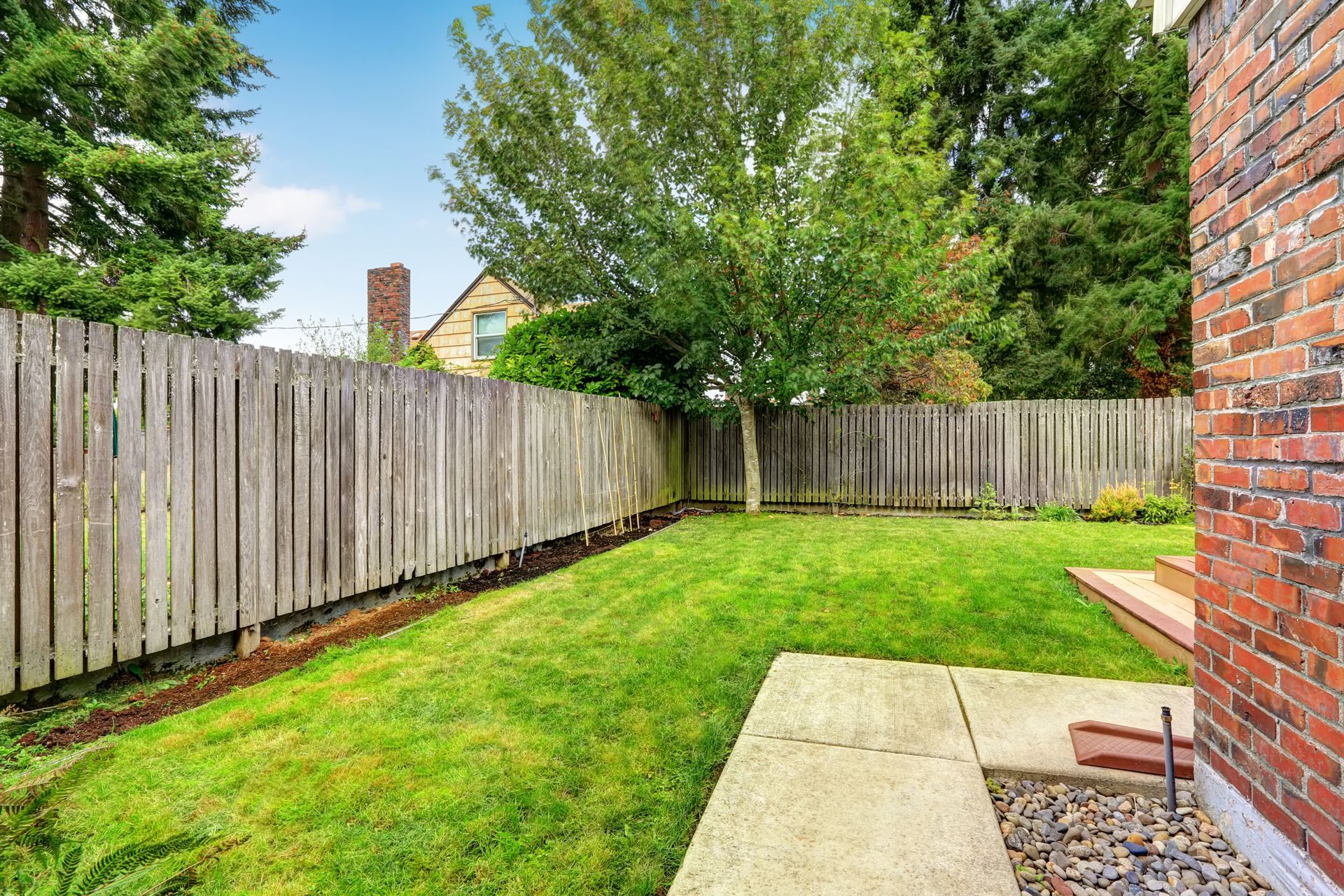 Small fenced backyard with green lawn, patio slab, and brick house wall