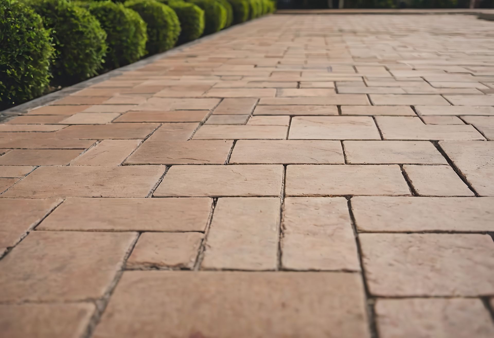 Stone walkway paved with rectangular tan tiles beside neatly trimmed green hedges