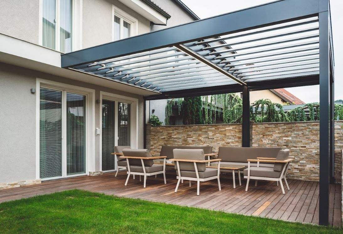 Modern patio with dining set under a gray pergola beside a house and lawn