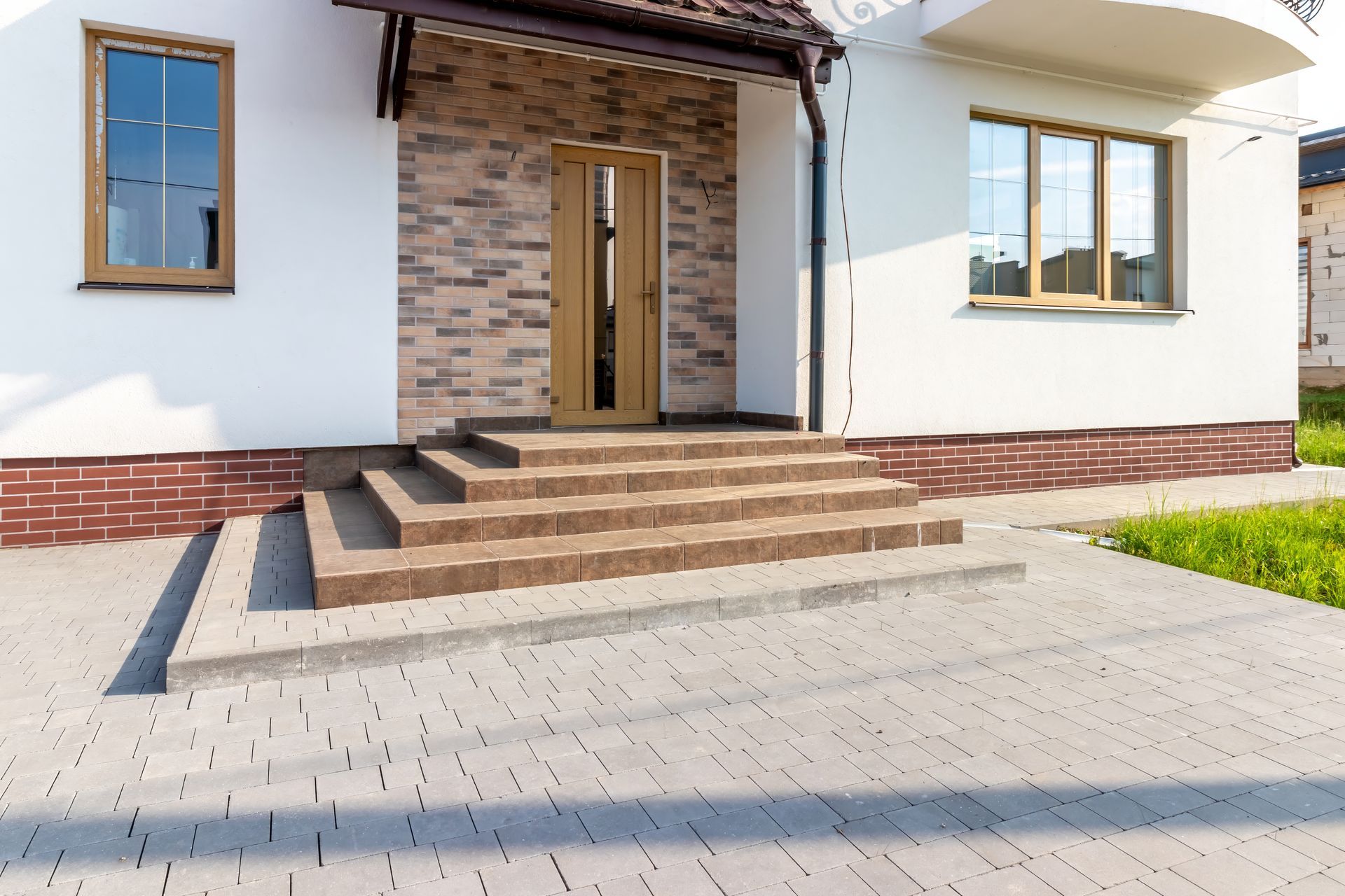 Front entrance of a modern house with brick steps, wooden double doors, and a paved driveway