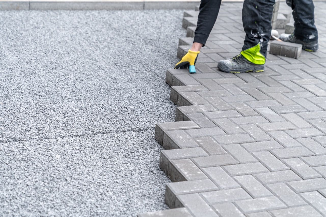 A man is laying bricks on a sidewalk.