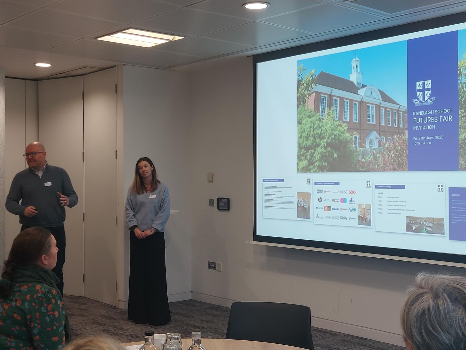 A man and a woman are giving a presentation in front of a large screen.