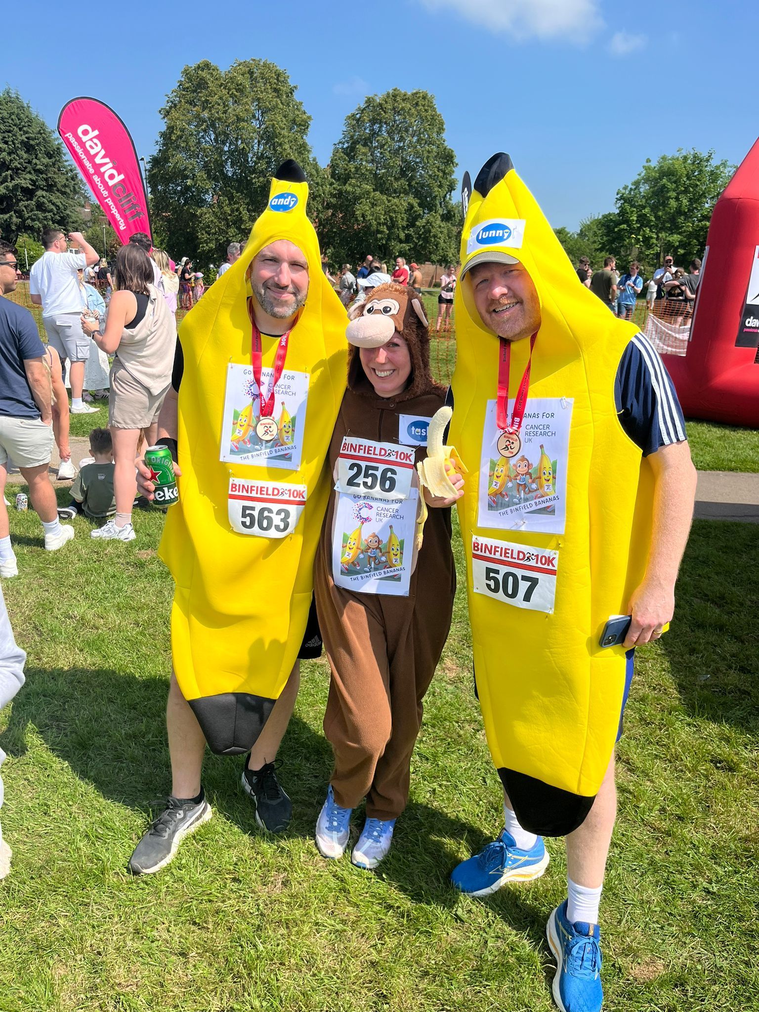 Three people in banana costumes are standing next to each other in a field.