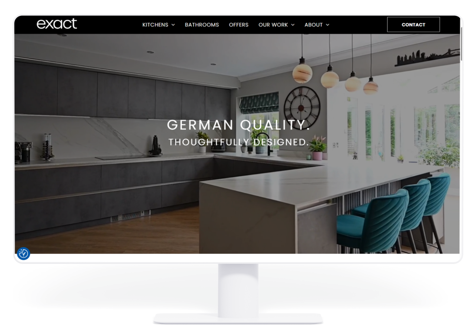 A monitor displays a website homepage featuring a modern, dark-toned kitchen with an island and text, 