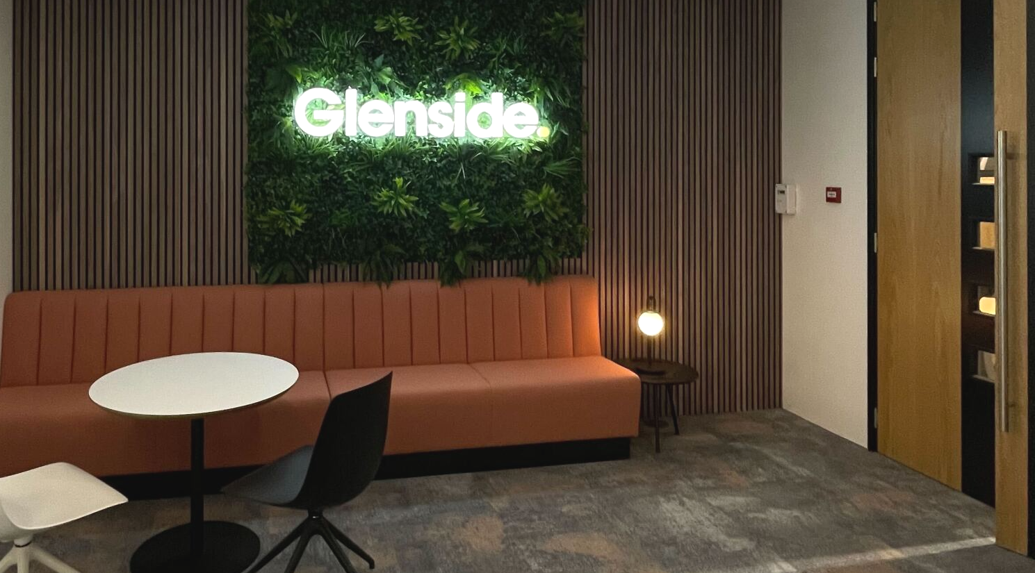 A room with a couch , table , chairs and a neon sign that says glenside.