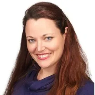 Headshot of a smiling person with long reddish-brown hair and blue eyes, wearing a dark blue top against a white background.