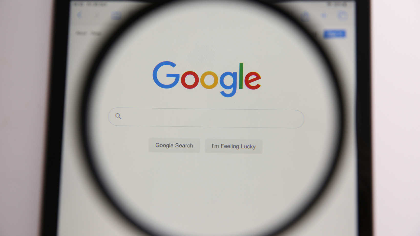 A magnifying glass is being used to look at the google search page on a cell phone.
