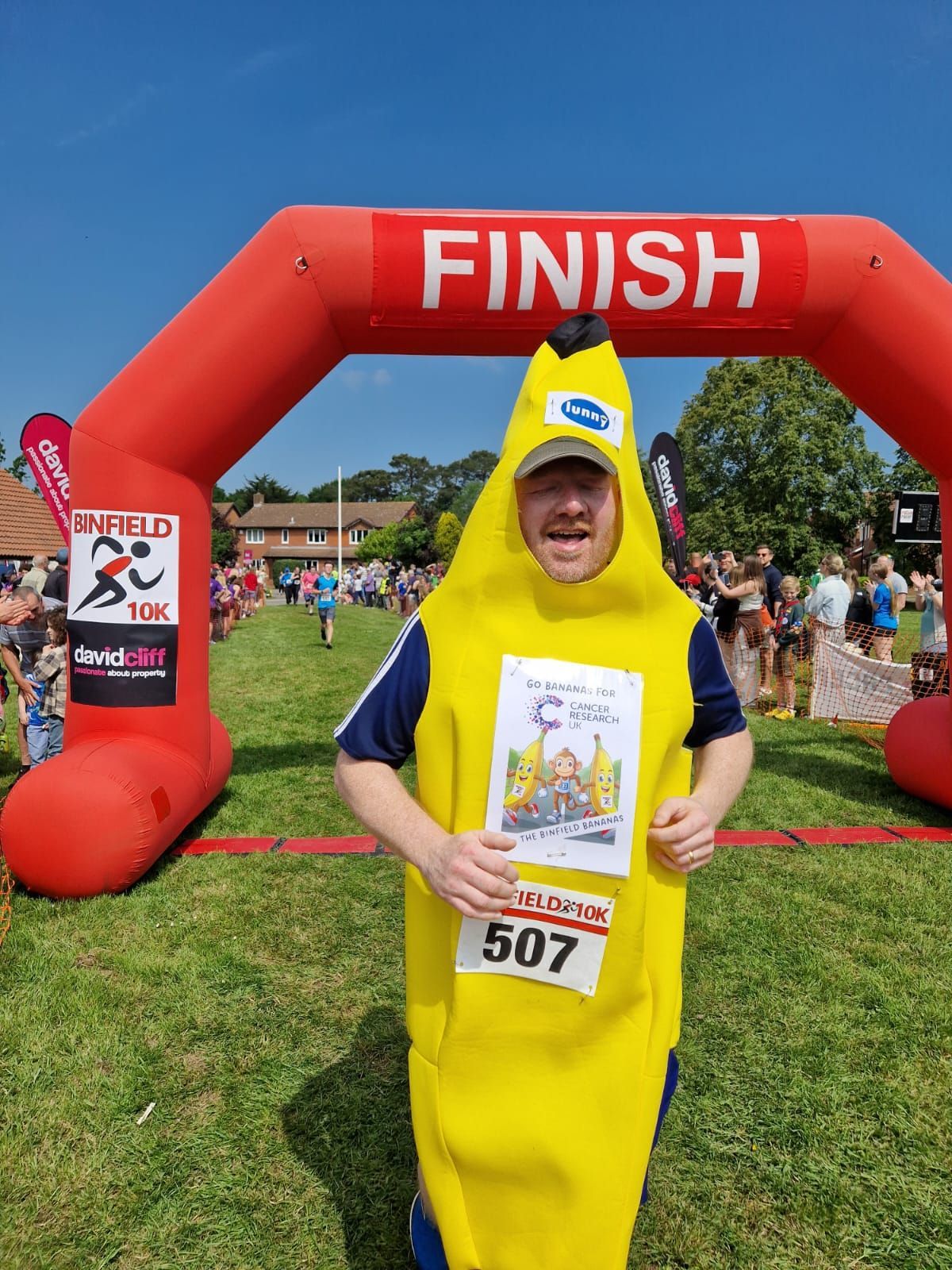 A man in a banana costume is standing in front of an inflatable finish line arch.