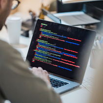 Person typing on a laptop displaying colorful code in a bright office setting