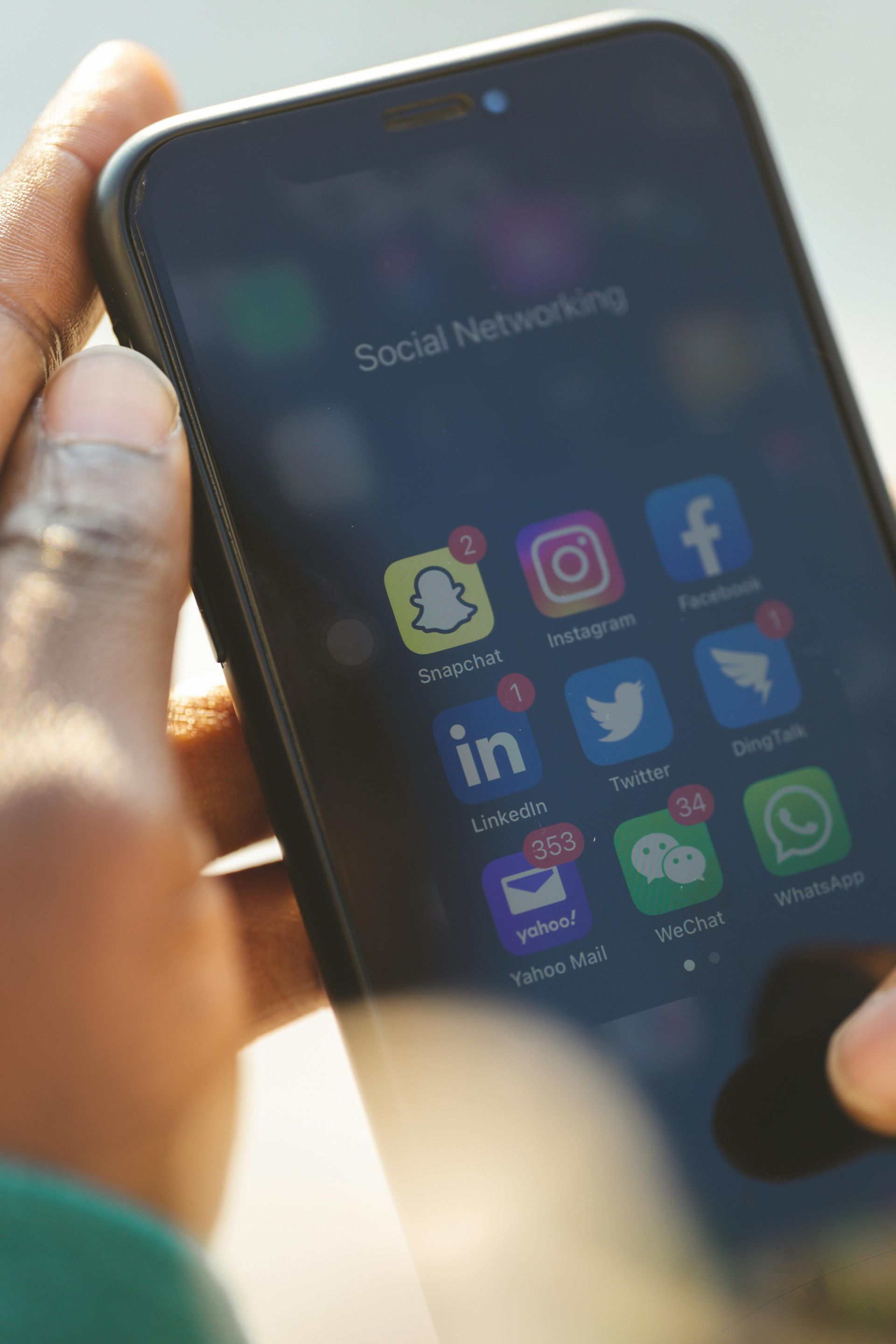 Person holding a smartphone, social media apps visible on screen: Snapchat, Instagram, Facebook, Twitter, WhatsApp.