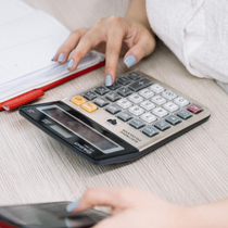Hand using a blue calculator on a wooden desk beside a receipt