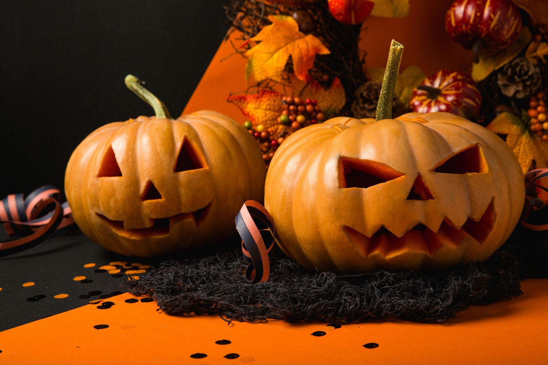 Two carved jack-o'-lanterns on a black and orange background. Halloween decorations with fall foliage.