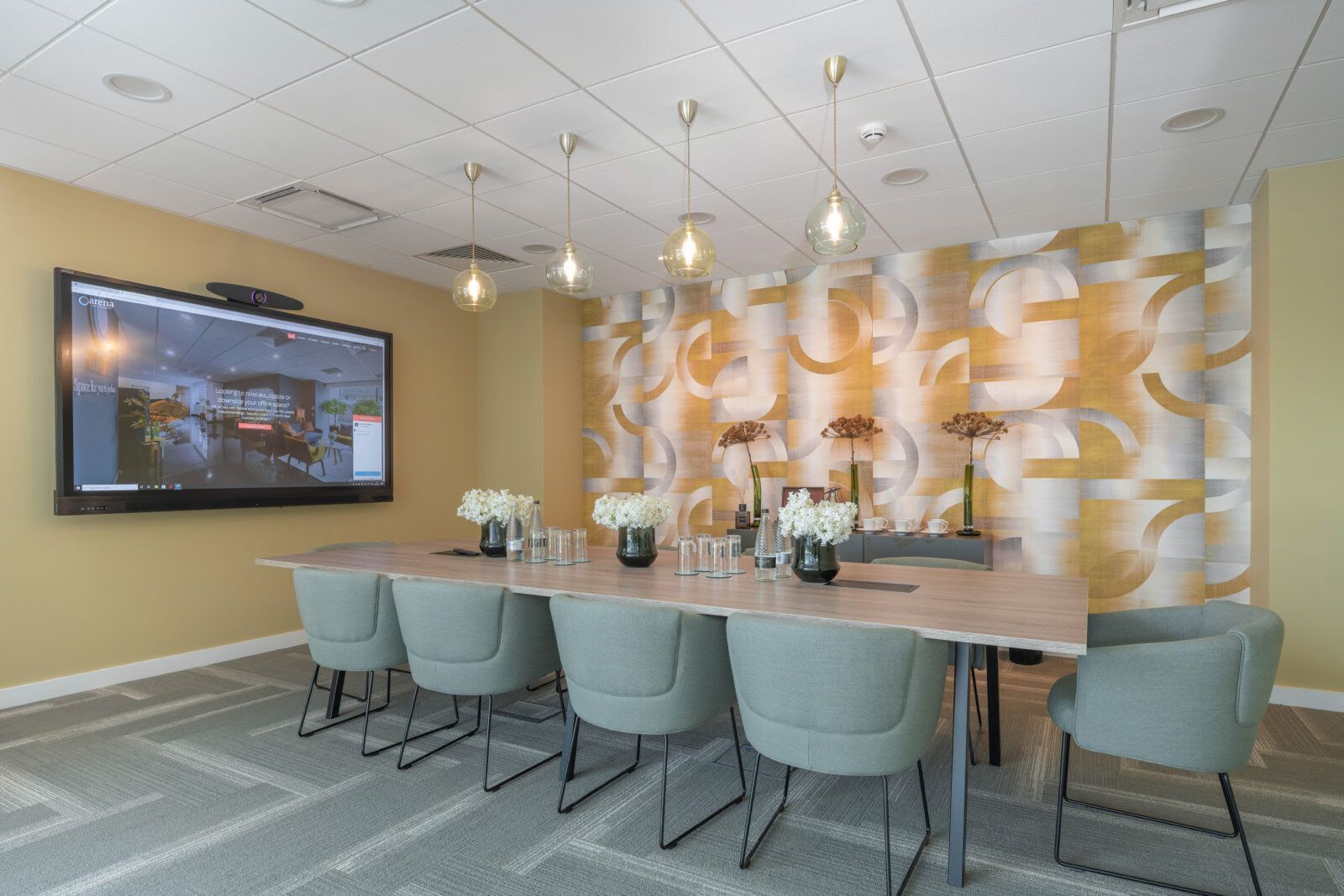 A conference room with a long table and chairs and a large screen on the wall.