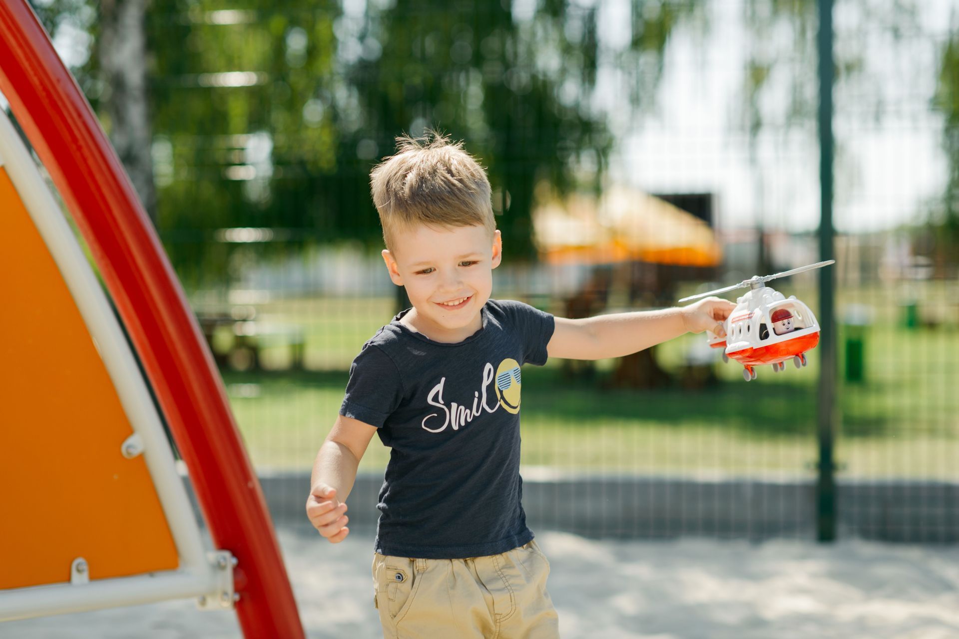 Child holding a toy truck on a playground, smiling beside an orange play structure
