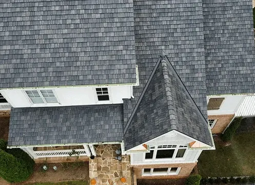 Aerial view of a house with a gray shingled roof and brick exterior, centered on a front porch.