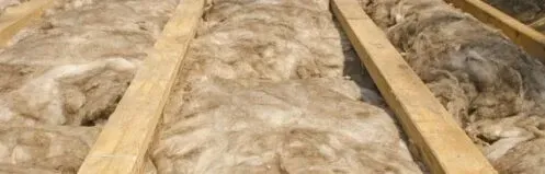 Bundles of insulation between wooden rafters in an attic ceiling
