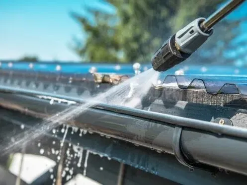 Water spraying from a hose onto a roof gutter during cleaning