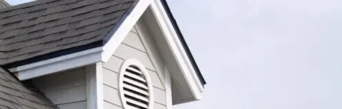 White house gable with vented attic window and gray shingles against a pale sky