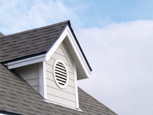 House roof dormer with white siding and a round louvered vent under a dark shingled roof