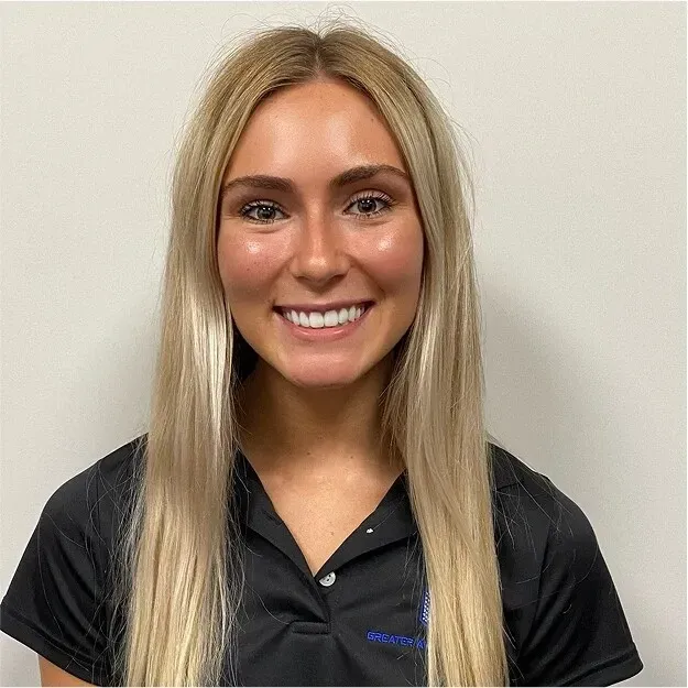 Smiling woman in a black polo shirt standing against a plain light wall
