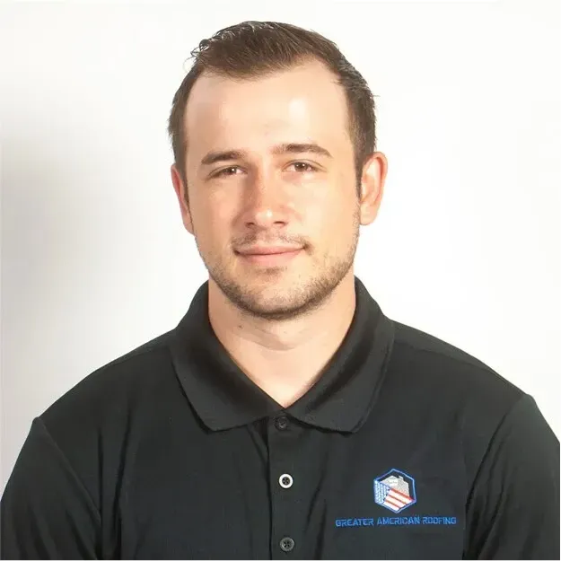 Portrait of a man in a black polo shirt with a company logo, standing against a white background
