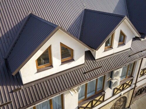 Aerial view of a house with dark gray roofs, white walls, and dormer windows.
